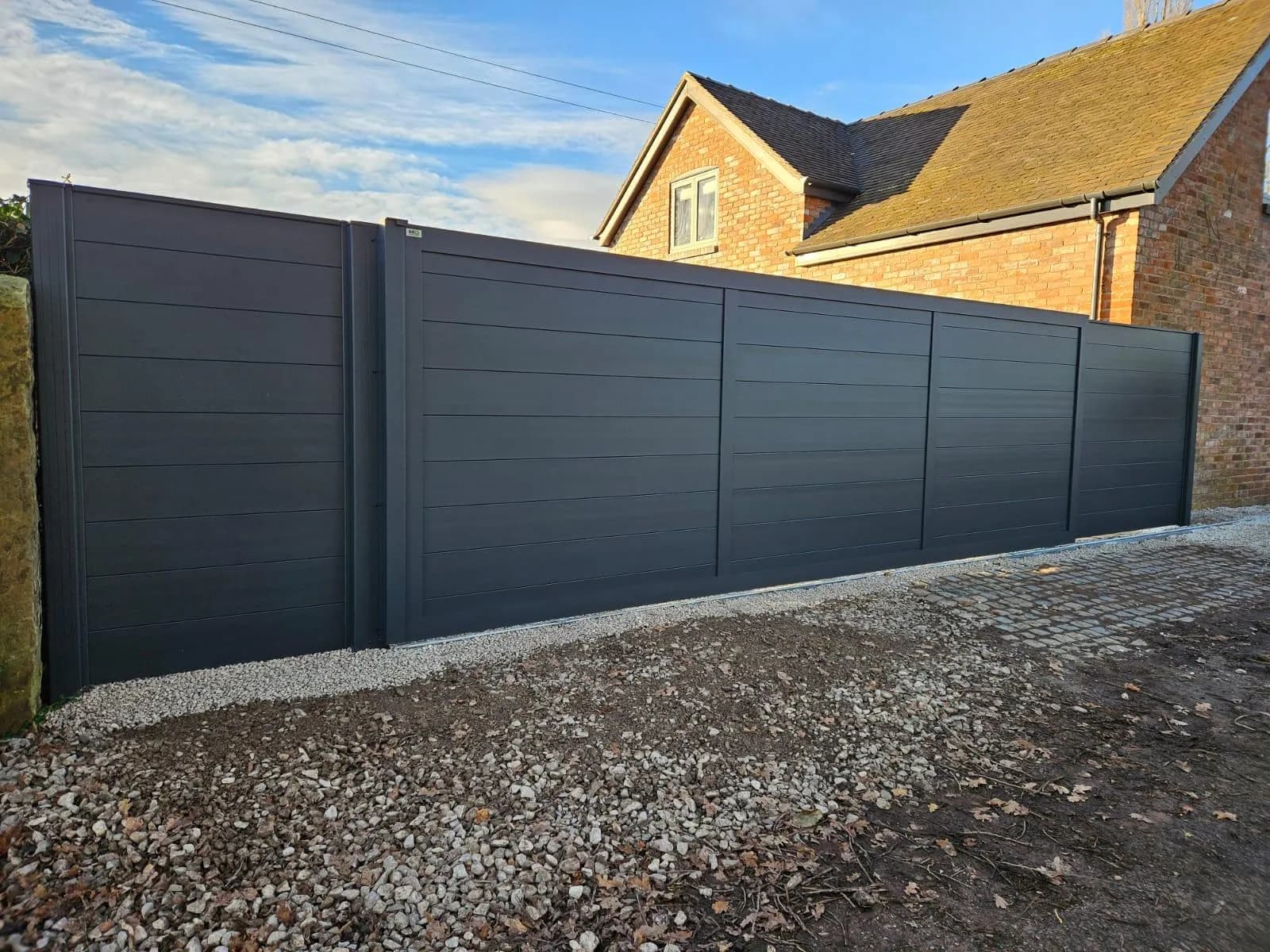 Full-height anthracite aluminium privacy fence along the boundary of a brick house