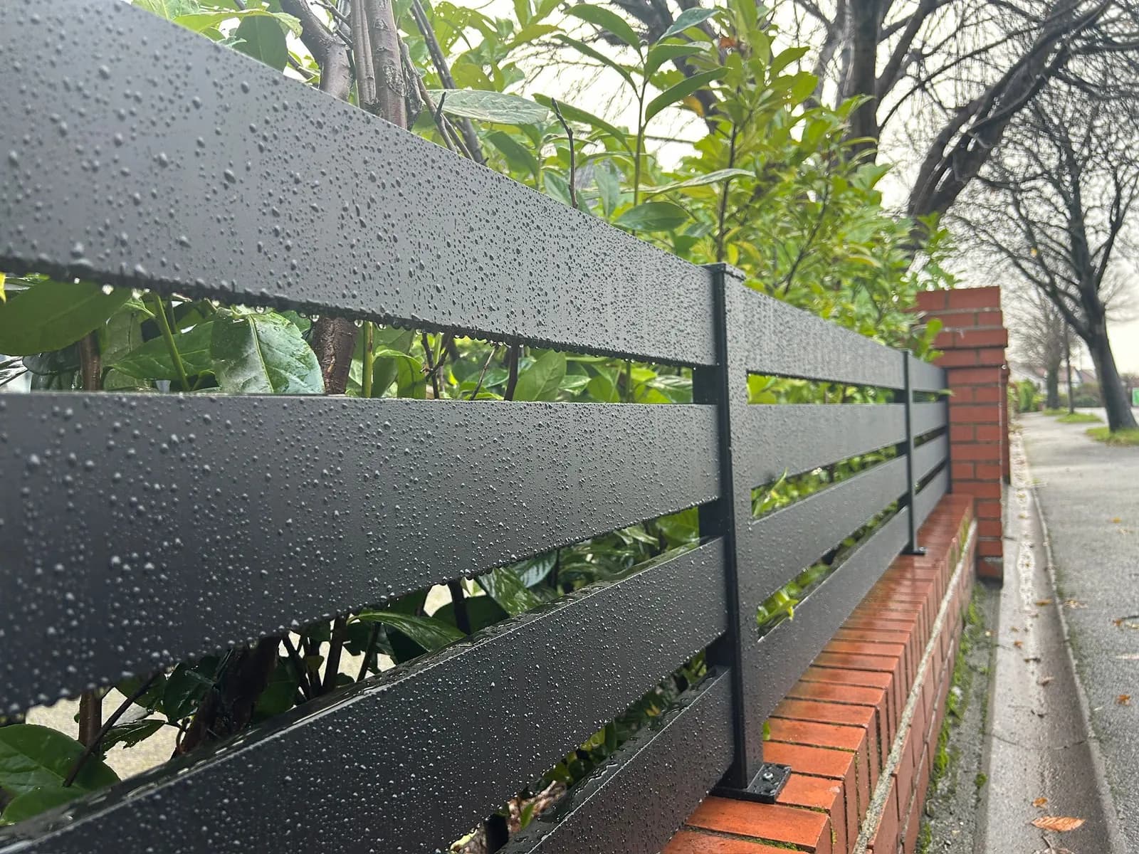 Rain droplets on anthracite powder coated aluminium fence slats above a brick wall
