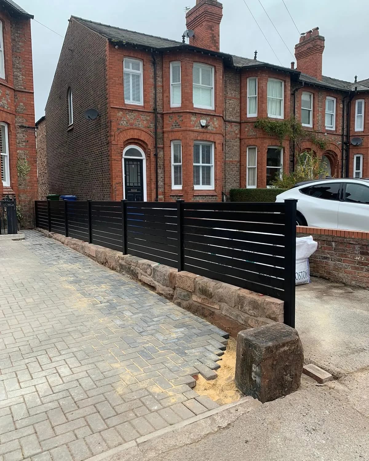 Anthracite slatted aluminium fence on a sandstone wall in front of a Victorian brick house