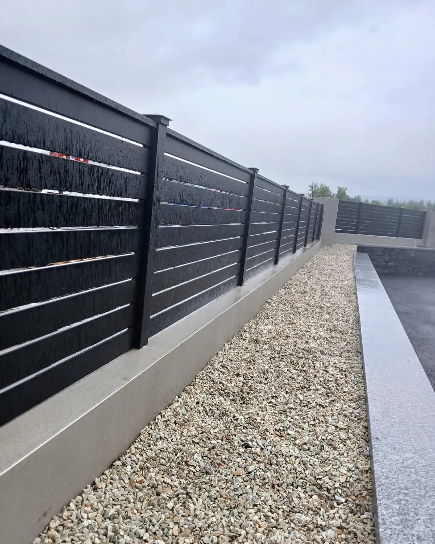 Long anthracite slatted aluminium fence on a wall above a gravel border
