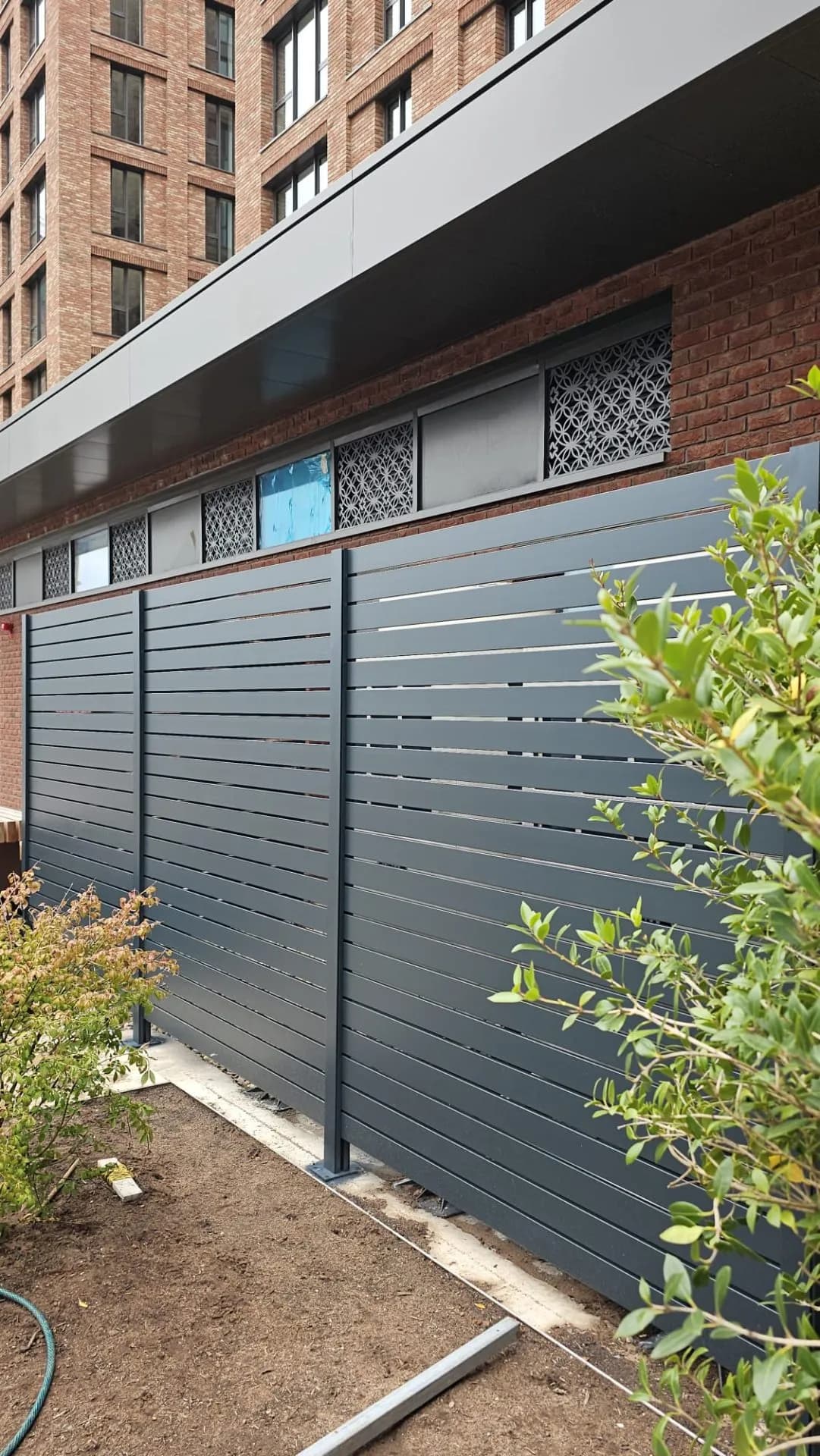 Anthracite slatted aluminium screen in a planted bed beside an apartment building