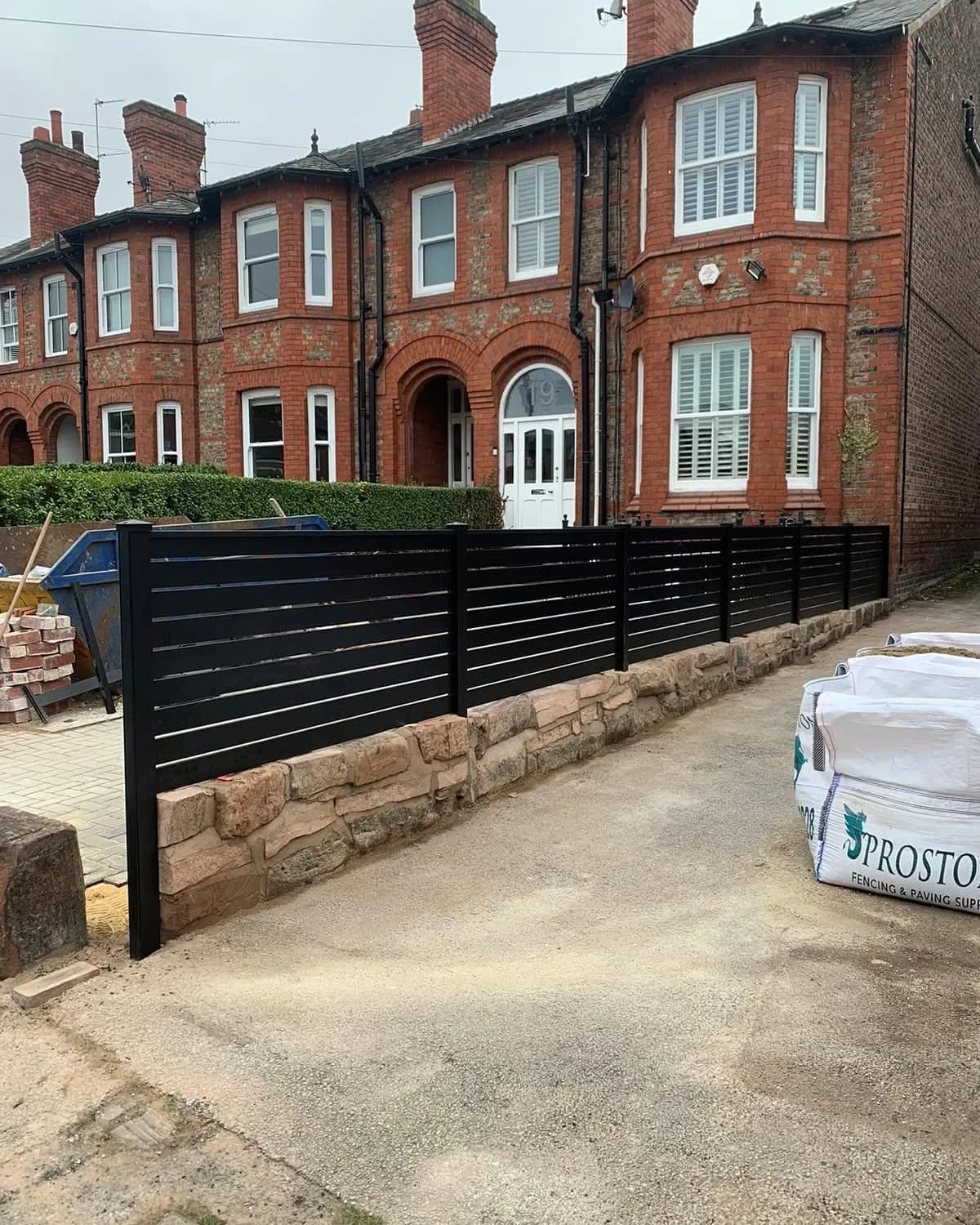 Low anthracite slatted aluminium fence on a stone wall outside Victorian brick houses