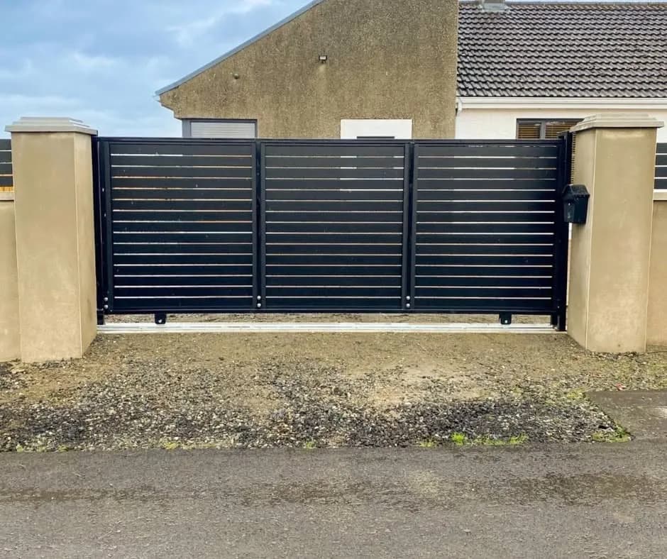 Anthracite slatted aluminium driveway gate between rendered pillars