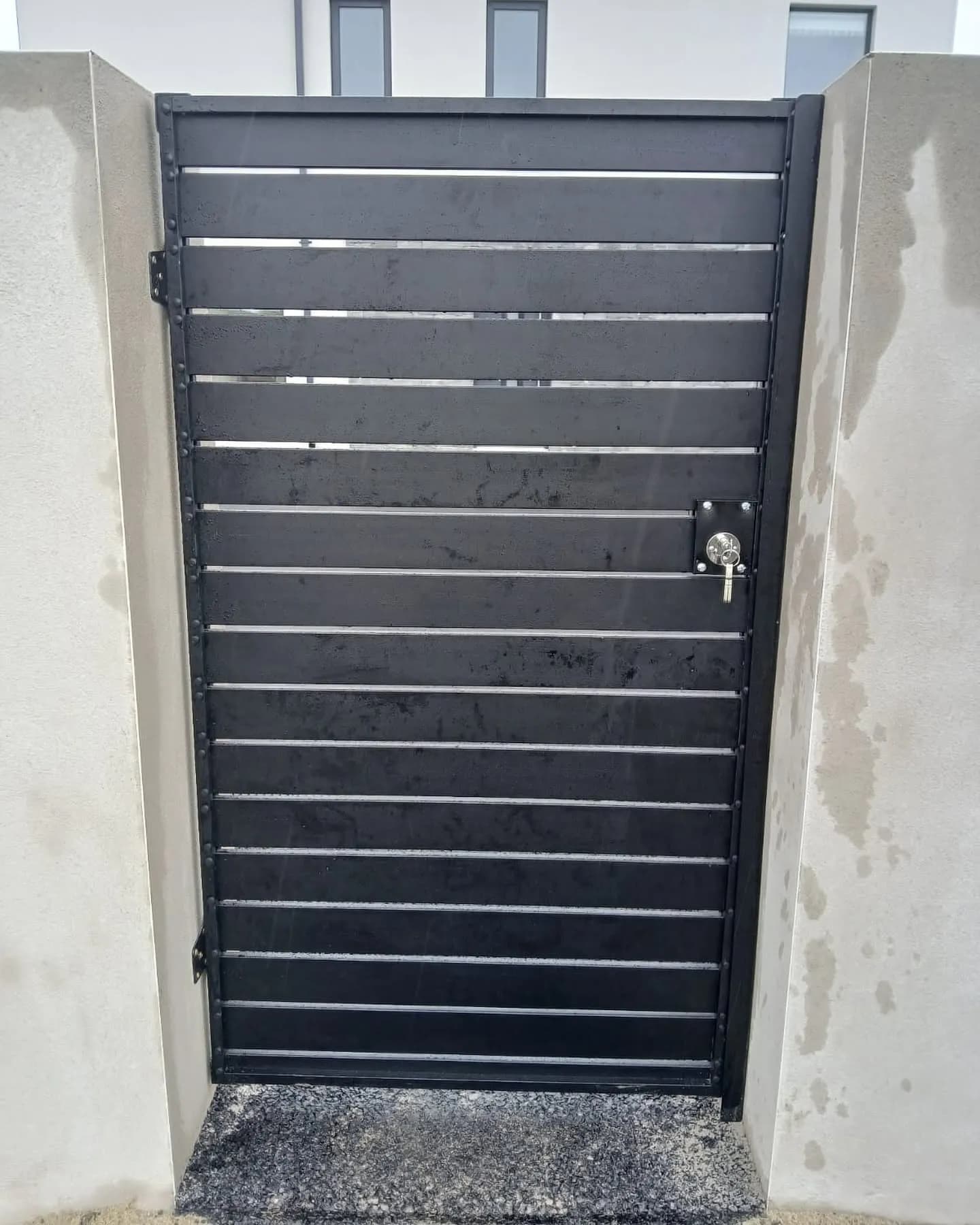 Anthracite slatted aluminium pedestrian gate set between rendered walls